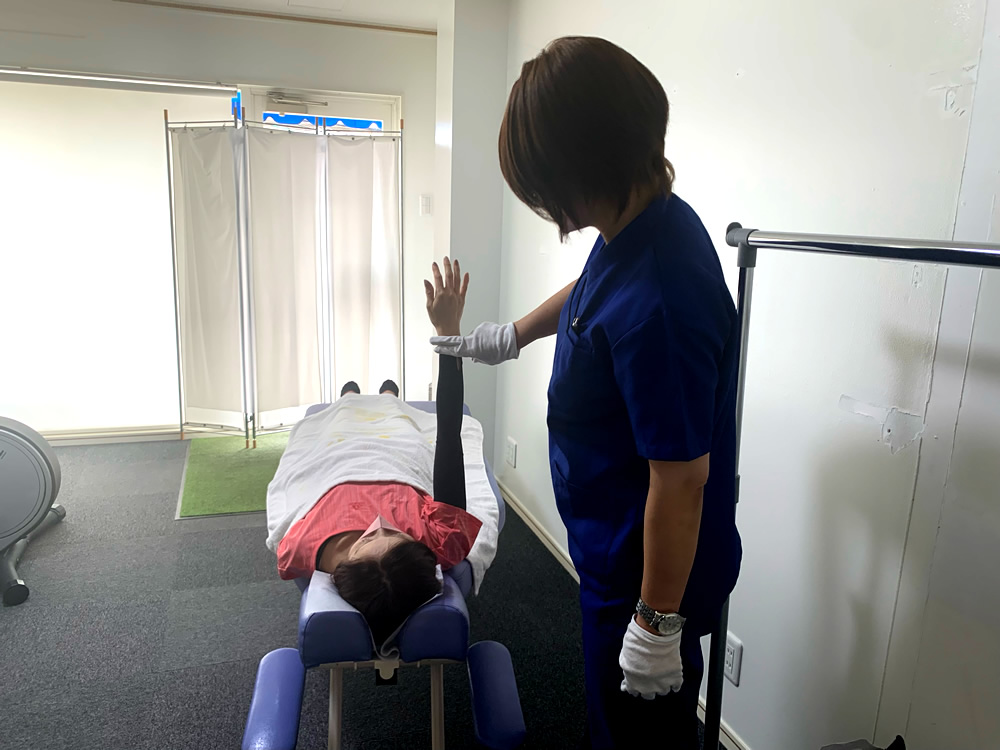 仰向けの女性の腕を院長が支えて施術している様子